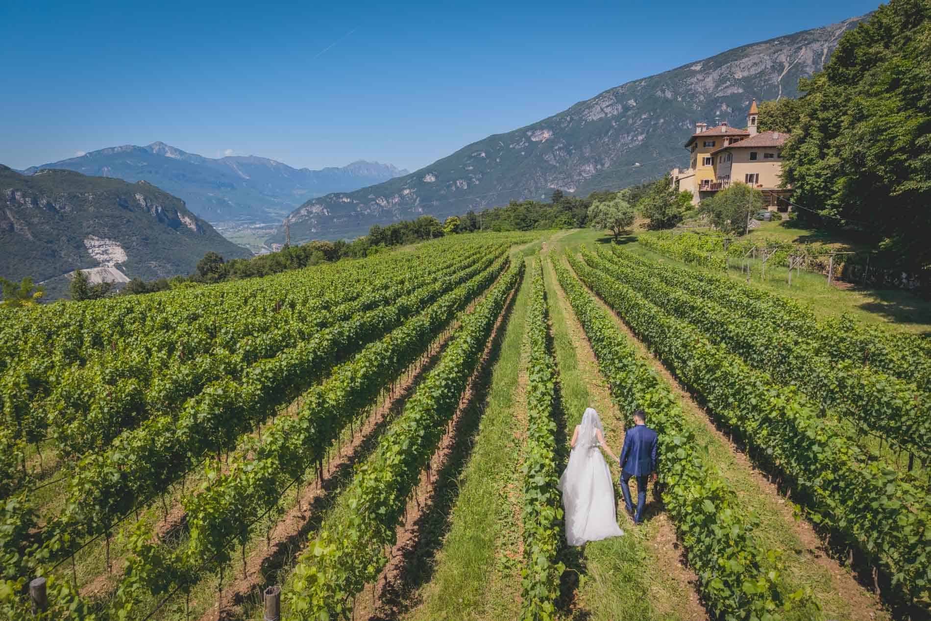 Bride and groom walking through lush vineyard in Trentino mountains.